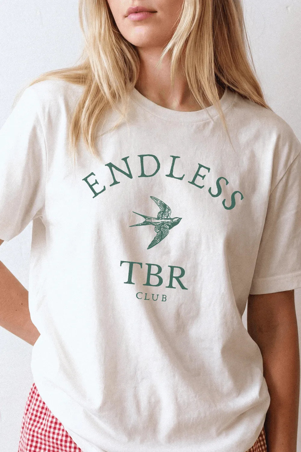 Woman wearing a cream bookish T-shirt with Endless TBR Club text and vintage swallow illustration