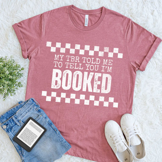book lover shiirt in heather mauve with bold white text reading “My TBR told me to tell you I’m BOOKED” styled with denim for cozy reader outfit