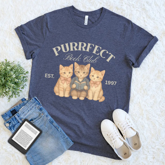 Flat lay of soft heather navy cat lover reader tee with cozy vintage feline design and "purrfect book club" text