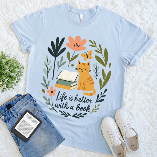 flat lay of light blue soft cotton t-shirt with "life is better with a book" text and cute cottagecore and cat design