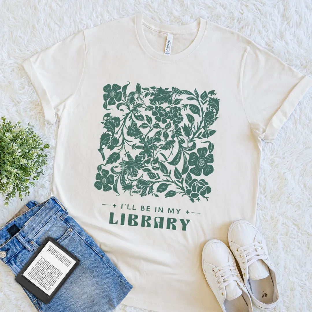 cream bookish shirt with muted green floral design and text 'I'll be in my library' on a light background