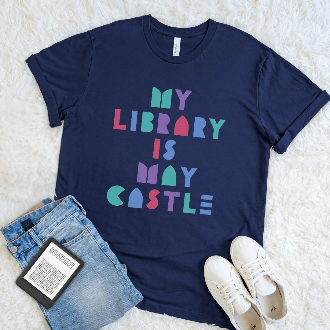 Navy book lover T-shirt with bright My Library Is My Castle typography styled with jeans and an e-reader.