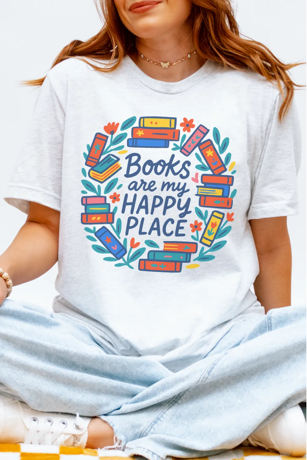 woman wearing soft cotton literary shirt with vibrant books and botanical elements with “Books are my happy place” text