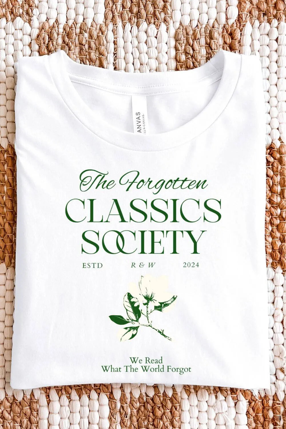 White soft cotton t-shirt with dark green serif typography reading “The Forgotten Classics Society” and a vintage botanical illustration in a dark academia aesthetic, folded on textile surface