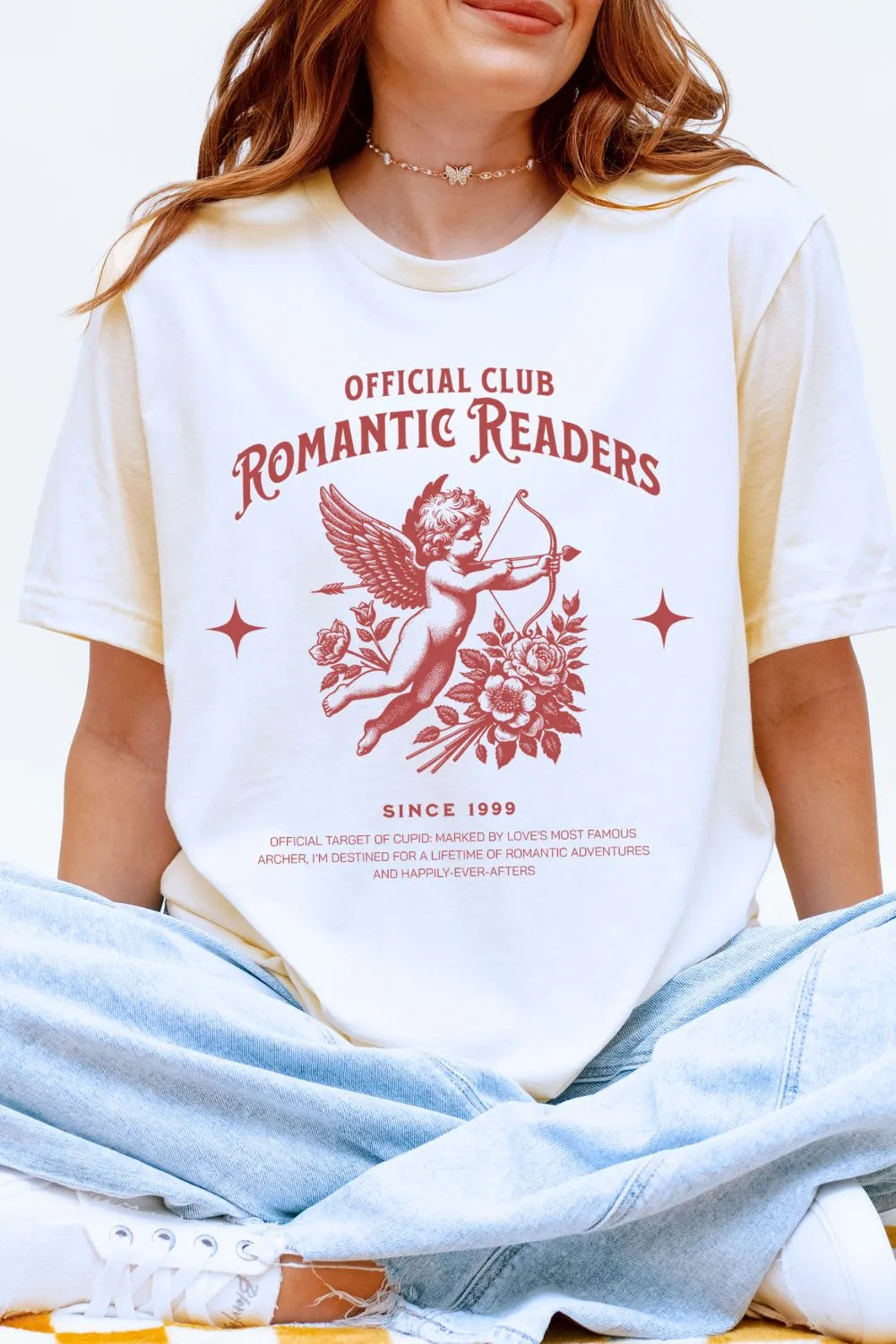 A white soft cotton t-shirt with red vintage Cupid illustration and text 'Official Club Romantic Readers' styled on a model wearing jeans in a cozy aesthetic