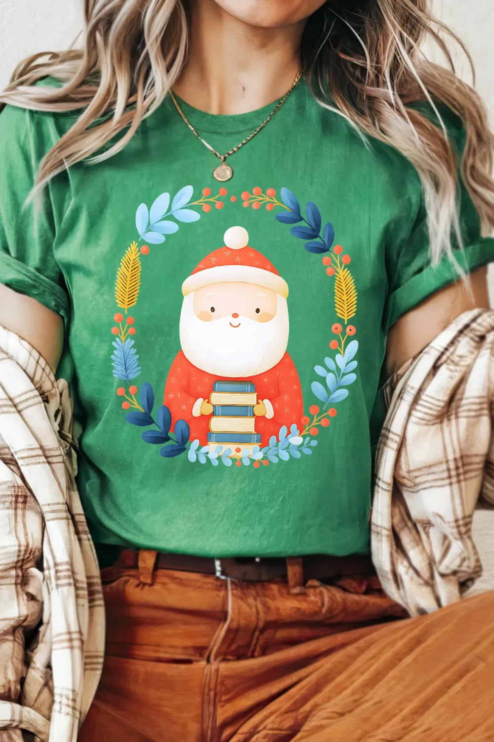 woman wearing green cozy Christmas t-shirt outfit featuring Santa holding books and botanical wreath design