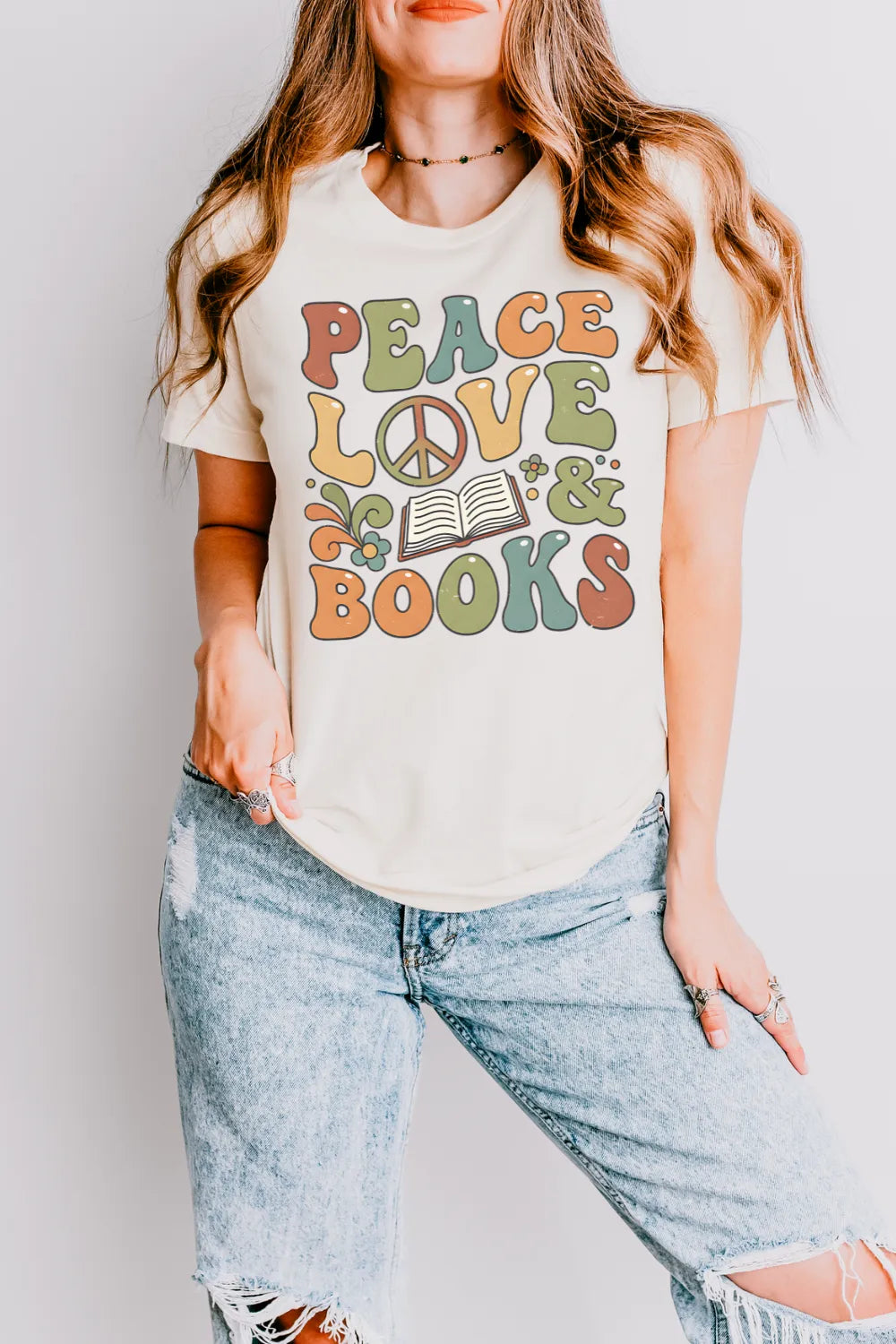 woman wearing cream groovy book shirt  with “Peace Love & Books” design and floral accents