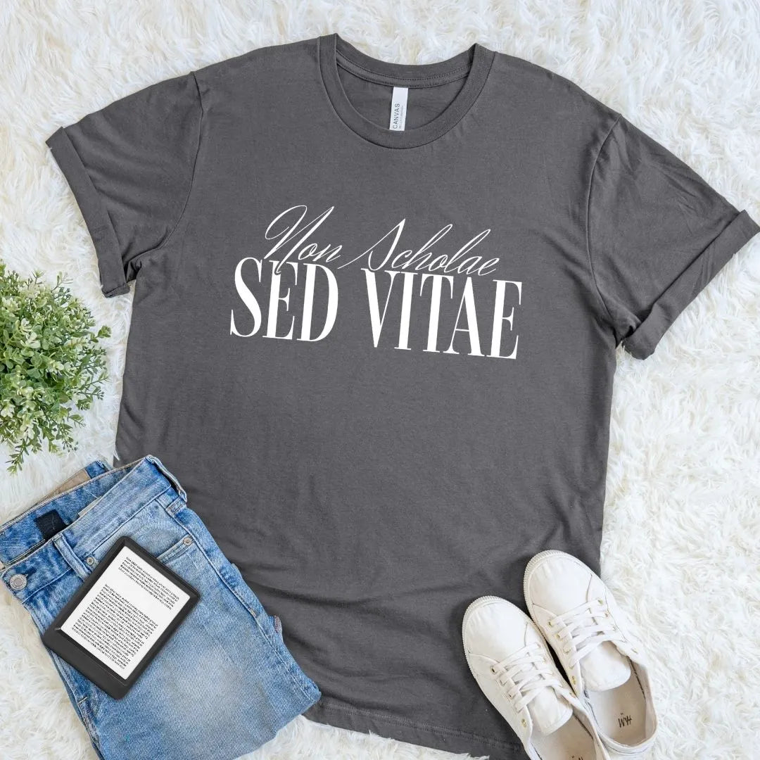 Soft cotton asphalt gray t-shirt with 'Non Scholae Sed Vitae' text, paired with jeans and sneakers on a light background