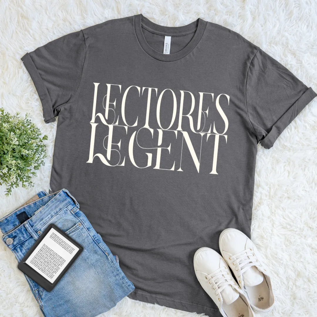 A dark gray graphic t-shirt for readers with the words 'LECTORES LEGENT' printed in a large cream serif font, styled in a flat lay on a white faux fur background with blue jeans, white sneakers, and a small potted plant.