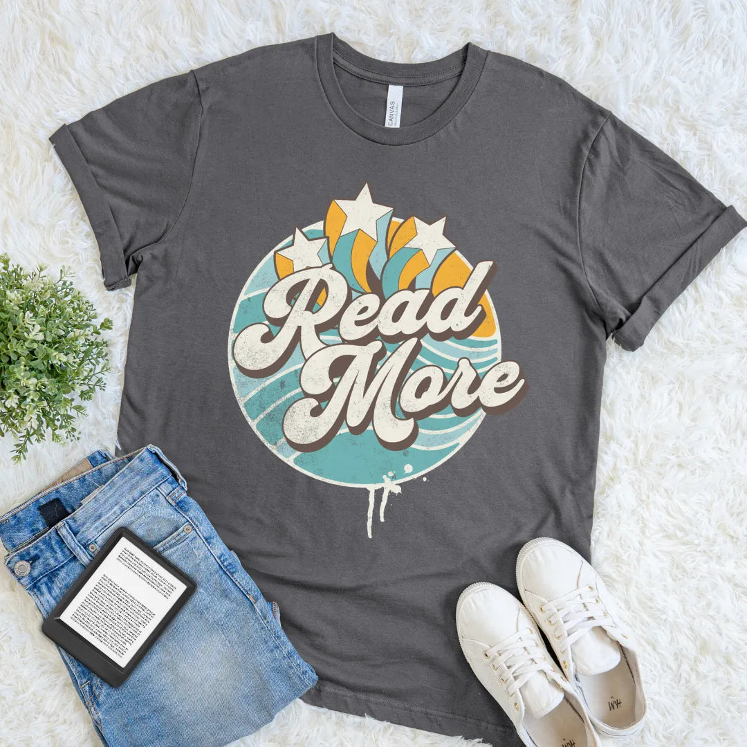 Asphalt “Read More” T-shirt with colorful retro typography, star accents, and a vintage burst design, a cheerful book lover graphic tee for readers.