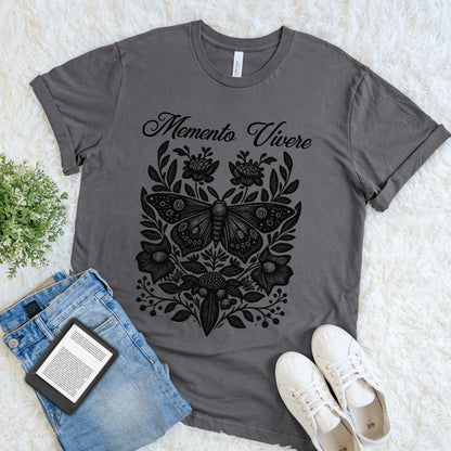 Gray t-shirt with black butterfly design and 'Memento Vivere' text, placed on a light surface with jeans and sneakers.