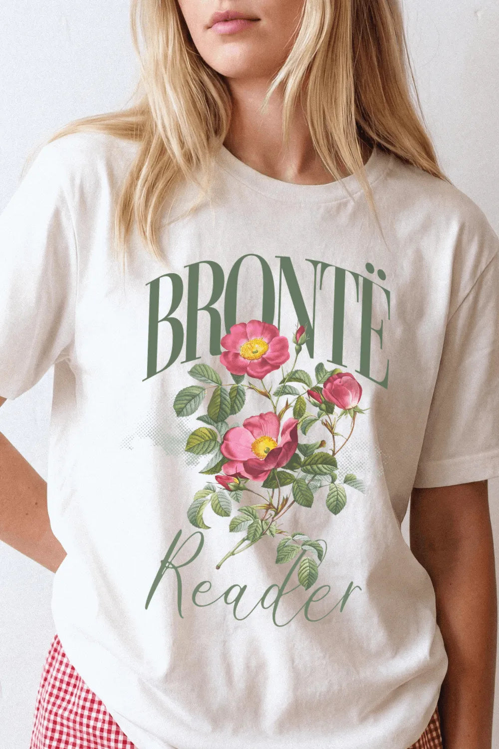Person wearing a cream bookish graphic t-shirt with vintage botanical roses and “Bronte Reader” typography, styled for light academia and cozy reading outfits