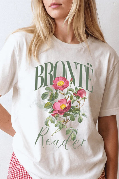 Person wearing a cream bookish graphic t-shirt with vintage botanical roses and “Bronte Reader” typography, styled for light academia and cozy reading outfits