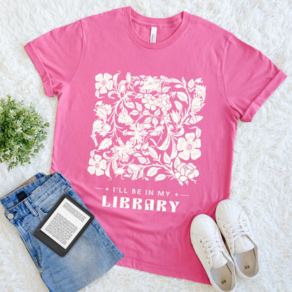 Book lover pink t-shirt with floral design and text, placed on a light surface with jeans, sneakers, and an e-reader for relaxed bookish outfit 