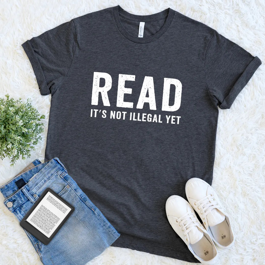 Dark Grey Heather “Read — It’s Not Illegal Yet” T-shirt with bold bookish lettering, a reader statement shirt centered on reading freedom and literary culture.
