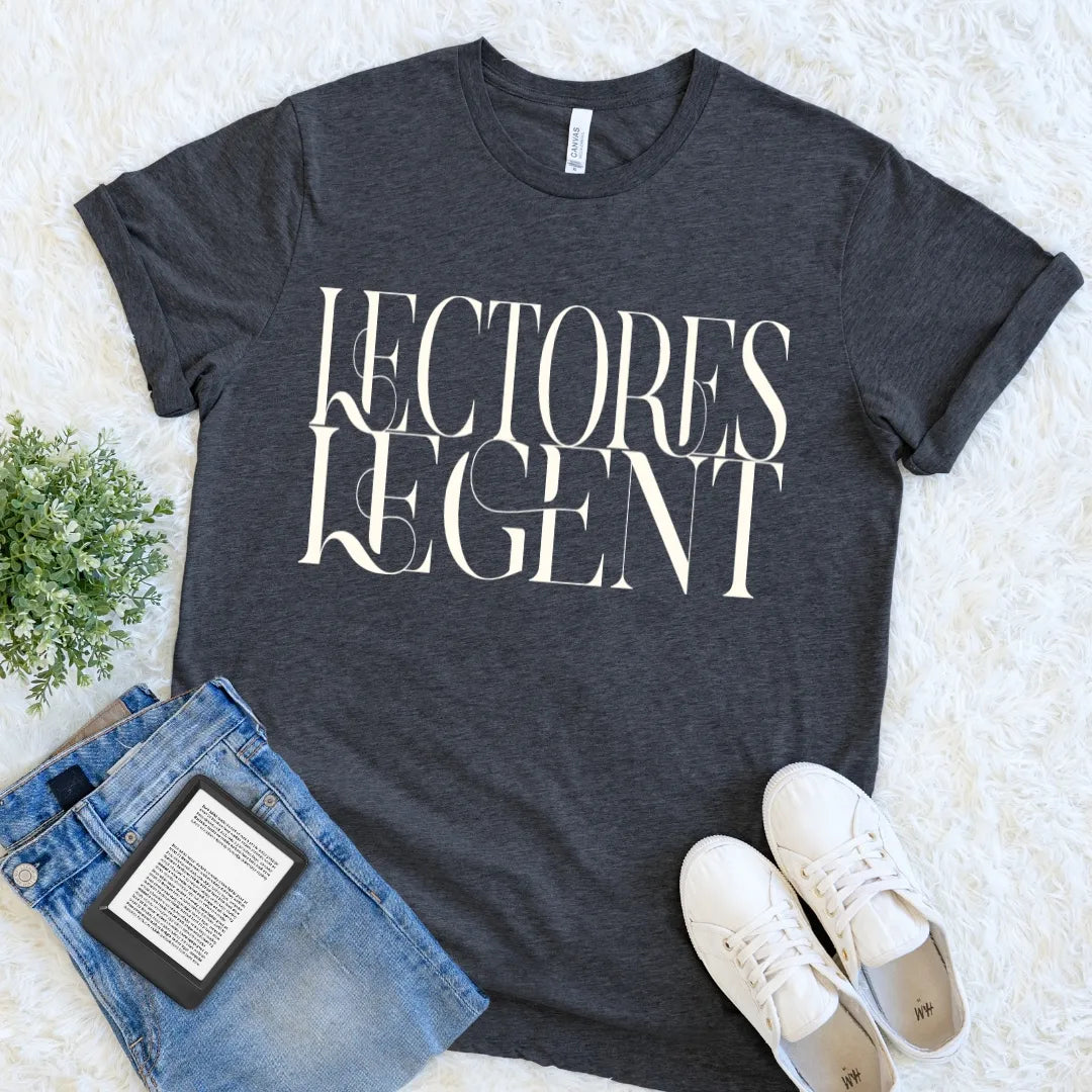 A dark heather gray bookish graphic t-shirt with the words 'LECTORES LEGENT' printed in large white serif letters, styled in a flat lay on a white faux fur background with blue jeans, white sneakers, and a small green plant.