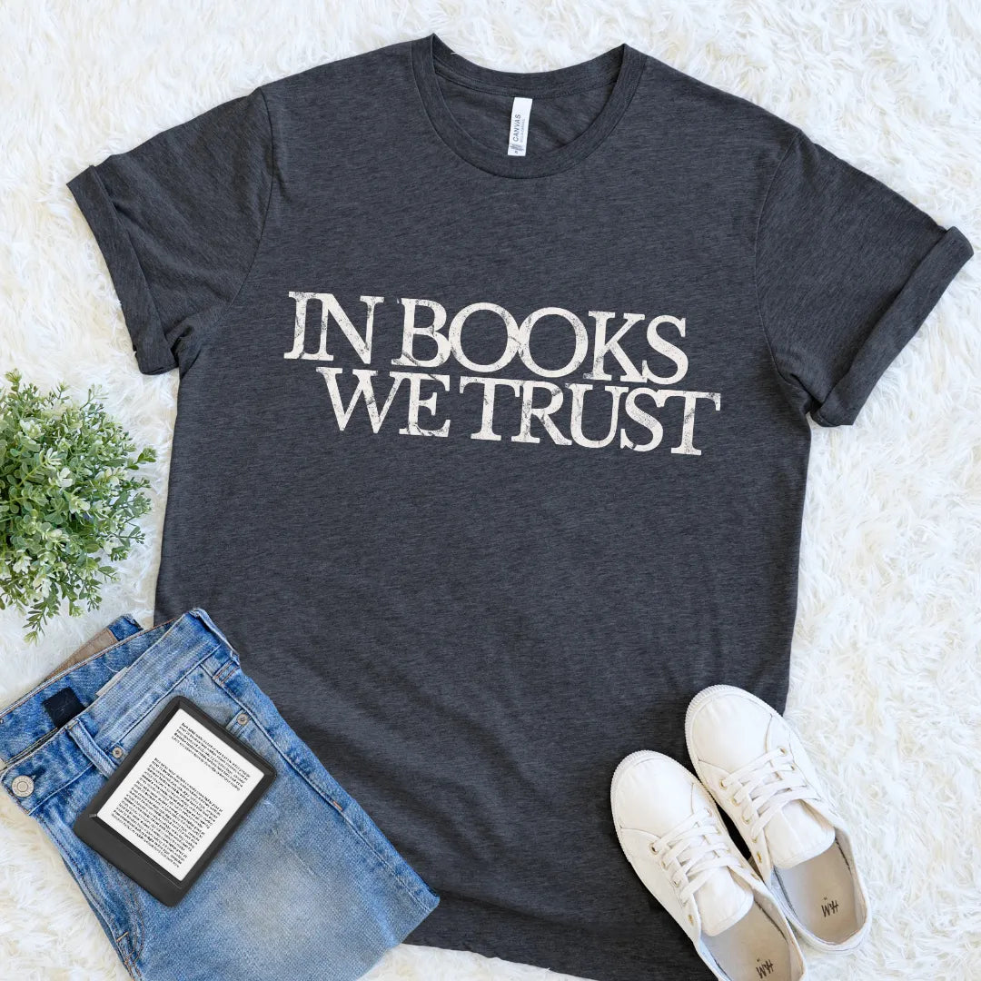 Dark gray reading t-shirt with 'IN BOOKS WE TRUST' text, paired with jeans and sneakers on a light background