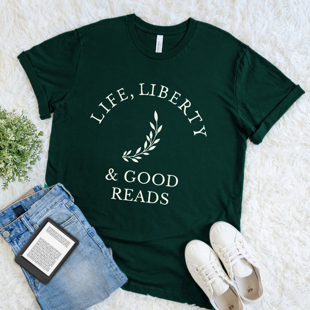 Forest green bookish t-shirt with 'Life, Liberty & Good Reads' text flat lay on a white surface with jeans and sneakers.