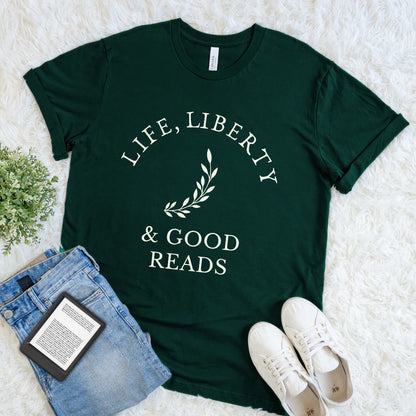 Forest green bookish t-shirt with 'Life, Liberty & Good Reads' text flat lay on a white surface with jeans and sneakers.