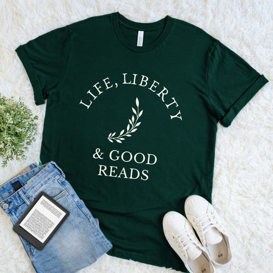 Forest green bookish t-shirt with 'Life, Liberty & Good Reads' text flat lay on a white surface with jeans and sneakers.