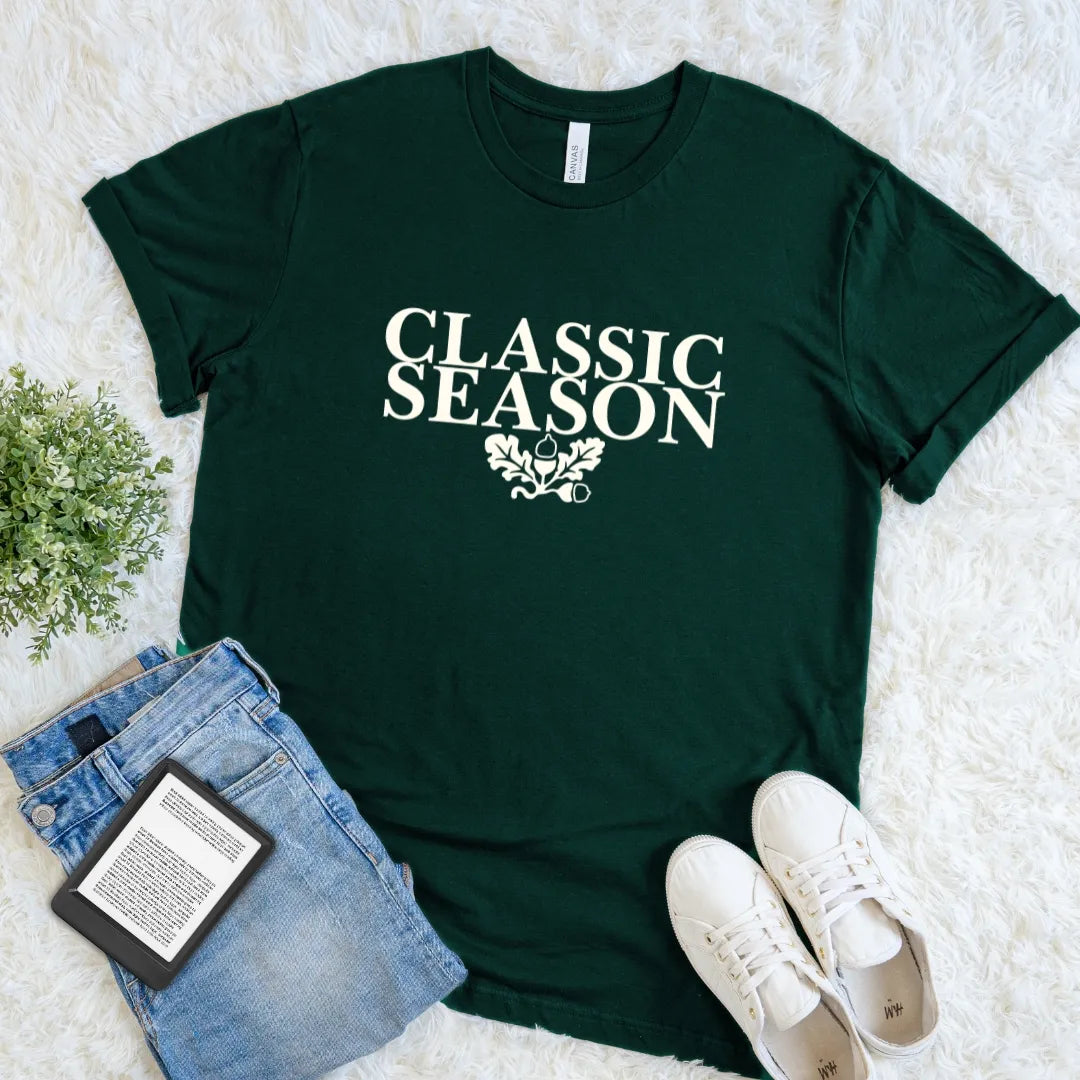 Forest green Classic Season book lover T-shirt with vintage cream serif typography, oak leaf and acorn details, a cozy autumn literary tee for classic readers.