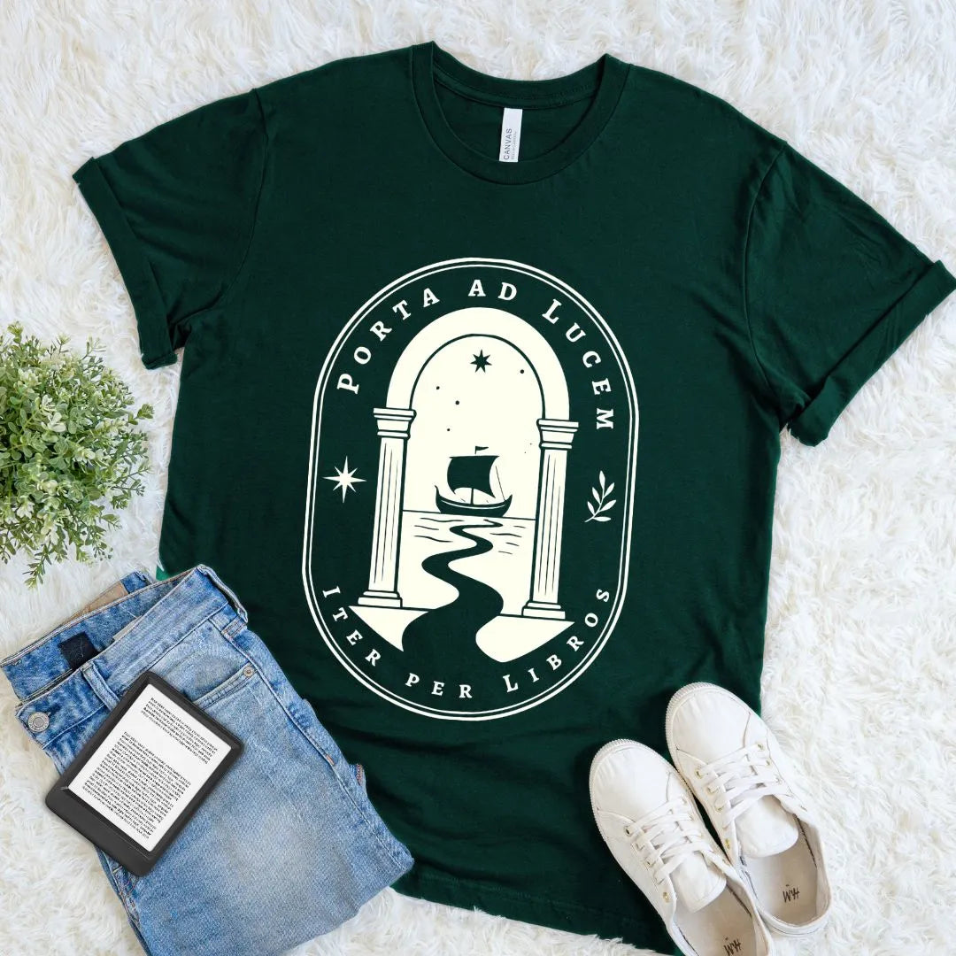 Forest Porta ad Lucem bookish T-shirt with ivory archway, sailing ship, stars, and Latin-inspired typography, a dark academia reader shirt styled flat with books.