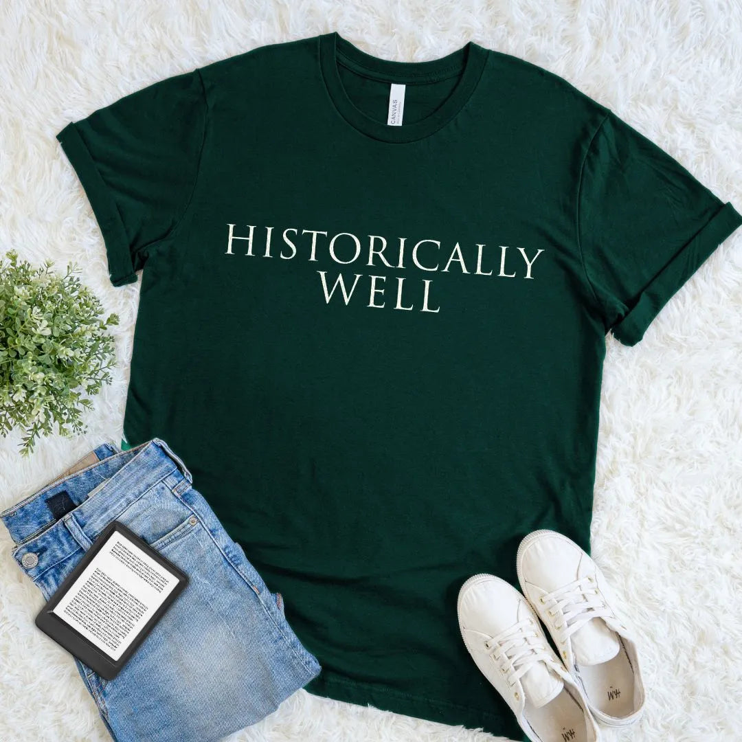 Forest green t-shirt with 'HISTORICALLY WELL' text on a light surface with jeans and sneakers.