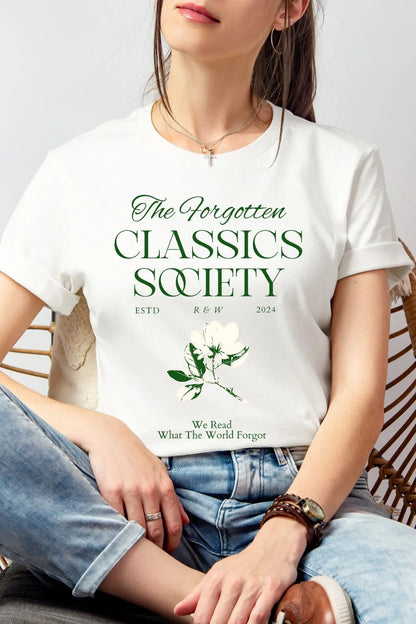 Woman wearing white soft cotton t-shirt featuring "Forgotten Classics Society" in elegant typography and a vintage botanical illustration, styled with denim for relaxed academia look