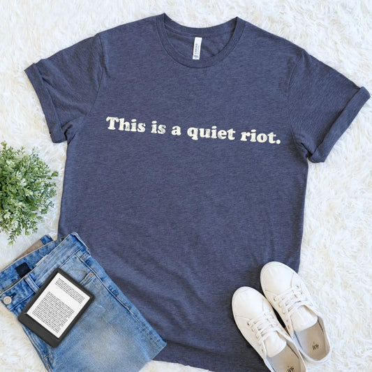 A heather navy blue graphic t-shirt with the reading slogan for book lovers  'This is a quiet riot.' printed in white across the chest.