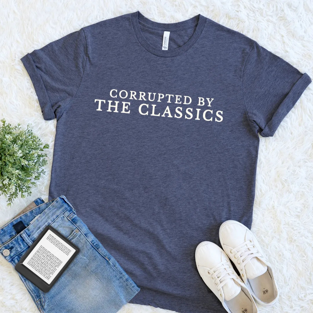 Heather navy blue bookish t-shirt with   Corrupted by the Classics quote in cream vintage serif typography paired with jeans and sneakers on a light background.