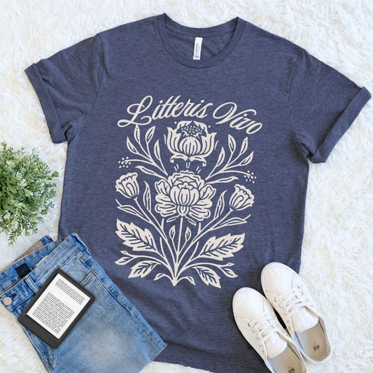 Heather navy Litteris Vivo botanical reader T-shirt with ivory Latin script, styled beside denim, sneakers, and an e-reader