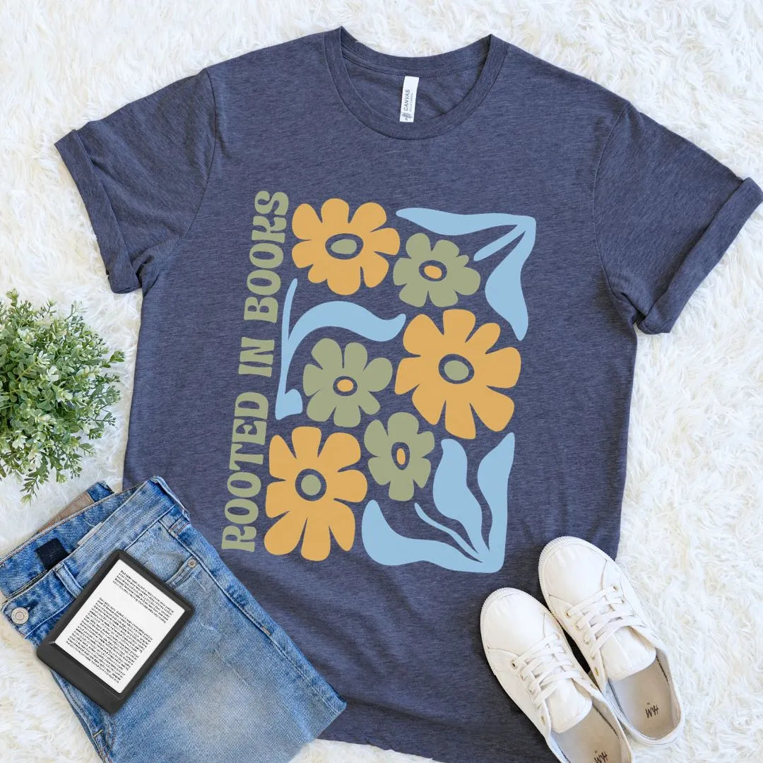 heather navy t-shirt with floral boho design and 'Rooted in Books' text, paired with jeans and sneakers on a light background.