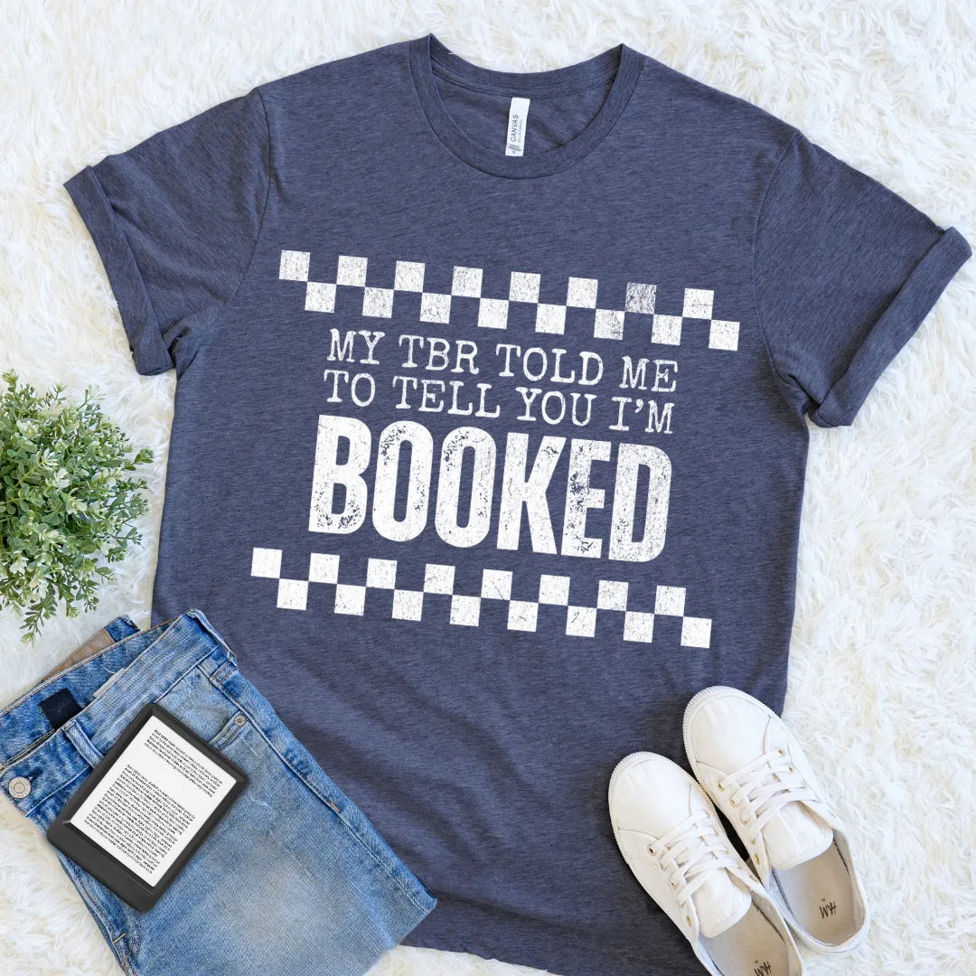 book lover shirt with bold white text reading “My TBR told me to tell you I’m BOOKED” styled flat lay with jeans and sneakers for relaxed bookish outfit