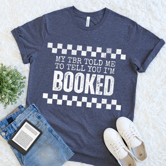 book lover shirt with bold white text reading “My TBR told me to tell you I’m BOOKED” styled flat lay with jeans and sneakers for relaxed bookish outfit