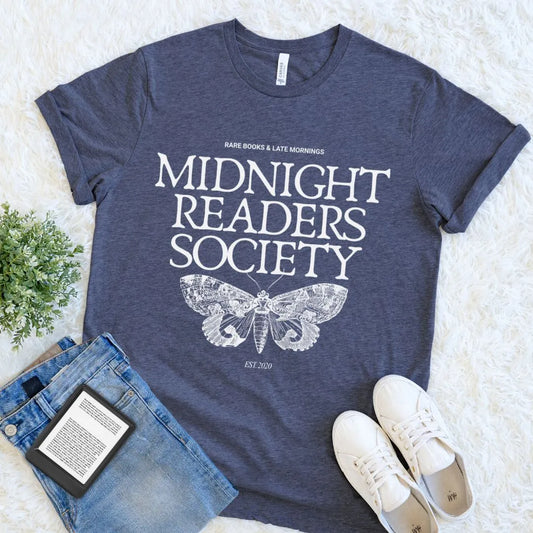 A heather navy t-shirt with vintage white text reading “Midnight Readers Society” and a detailed moth illustration, styled in a moody bookish aesthetic with jeans and sneakers 