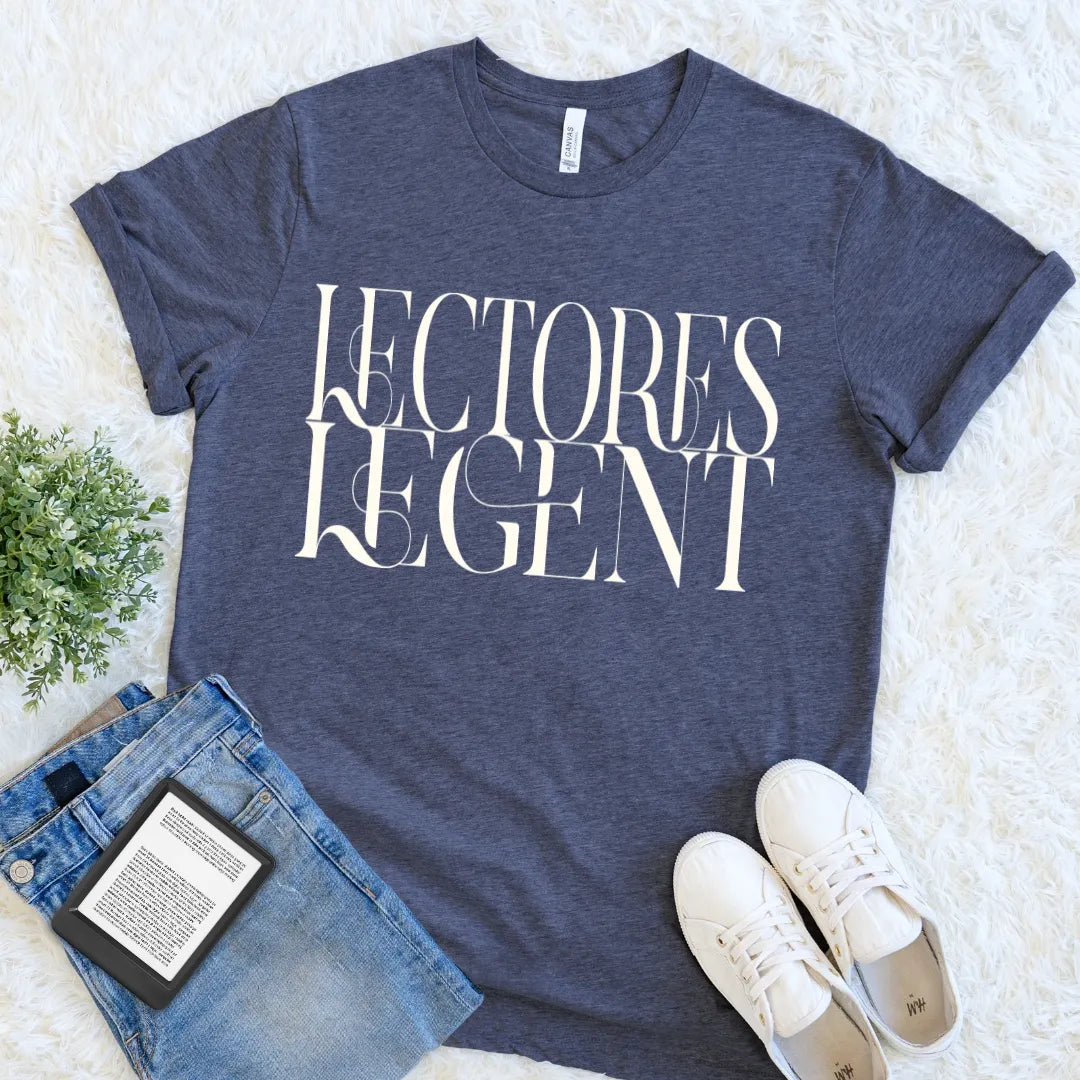 A heather navy blue graphic t-shirt for book lovers with the words 'LECTORES LEGENT' printed in large white serif letters, styled in a flat lay on a white faux fur background with blue jeans, white sneakers, and a small potted plant.