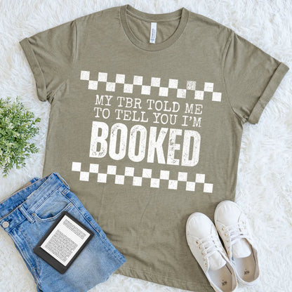 Book lover shirt in heather olive green with 'My TBR told me to tell you I'm booked' text, paired with jeans and sneakers for a cozy bookish style 