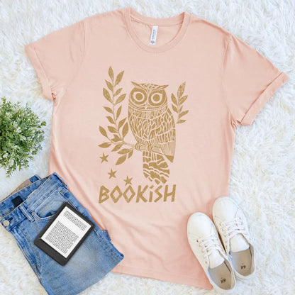  heather paech reader t-shirt with owl design and 'BOOKISH' text, paired with jeans and sneakers on a white surface.