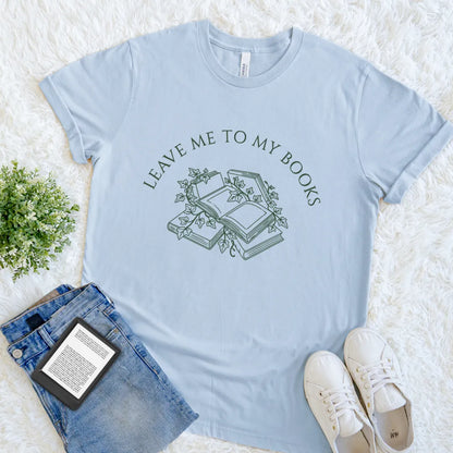 Light blue t-shirt with 'Leave me to my books' design on a white surface with jeans and sneakers.