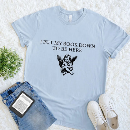 Soft cotton light blue reader shirt featuring vintage-style angel illustration  and text "I put down my book to be here"