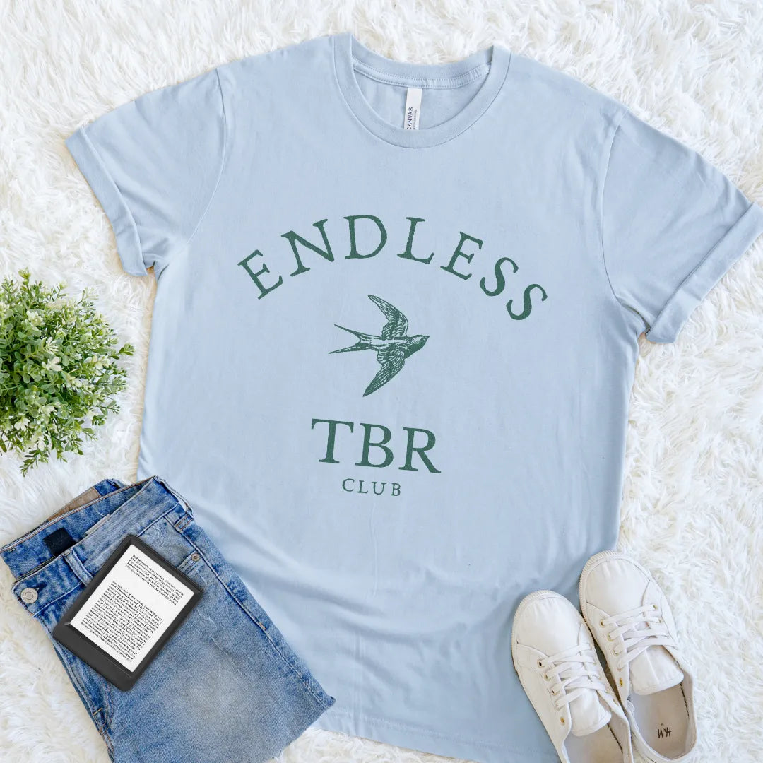 Light blue reader  t-shirt with 'Endless TBR Club' text and a swallow design, placed on a white surface with jeans and sneakers.