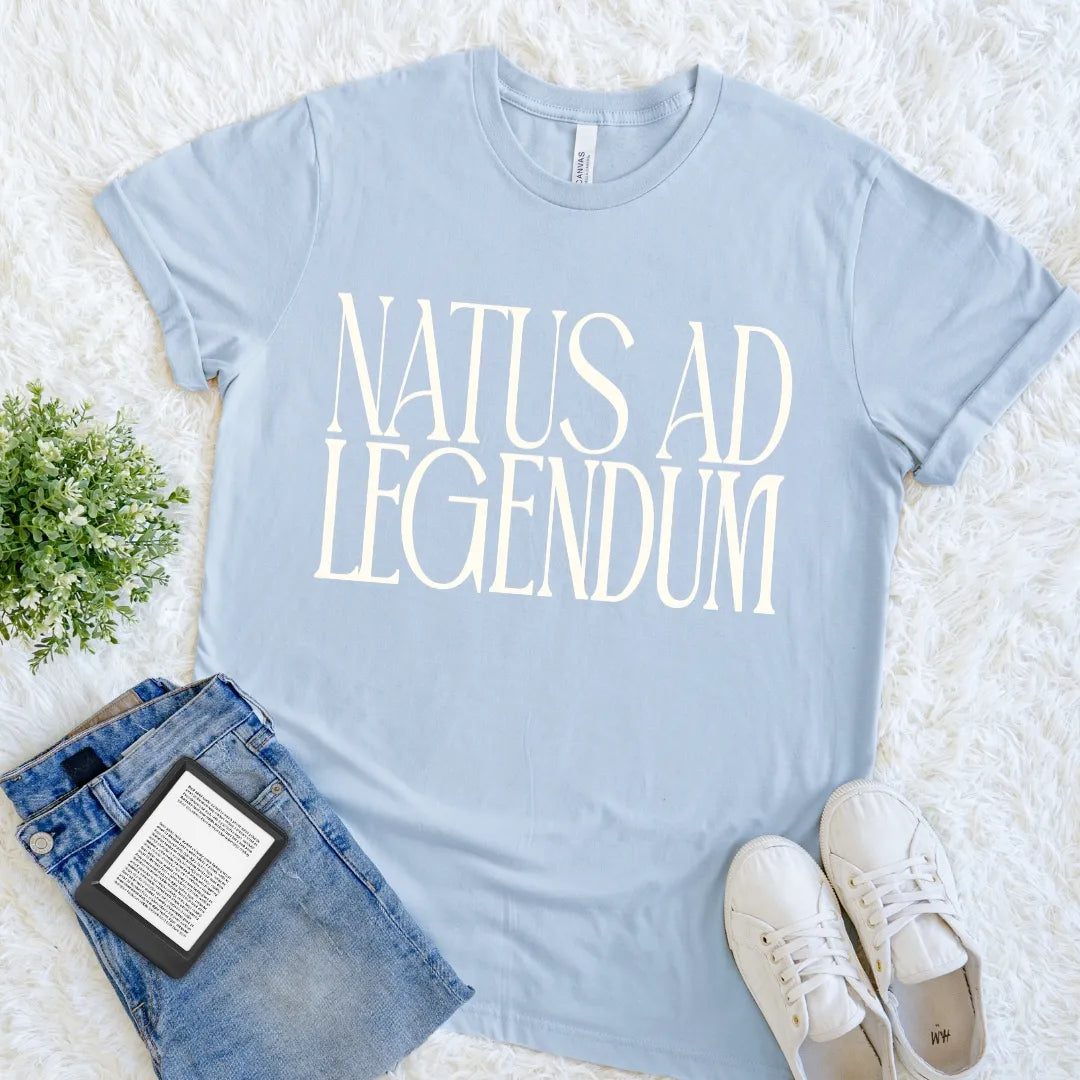 Light blue bookish T-shirt with Natus ad Legendum Latin phrase in oversized cream serif typography.