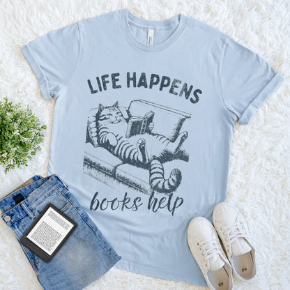 Light blue bookish tee featuring cat reading on a couch illustration and “Life Happens Books Help” text