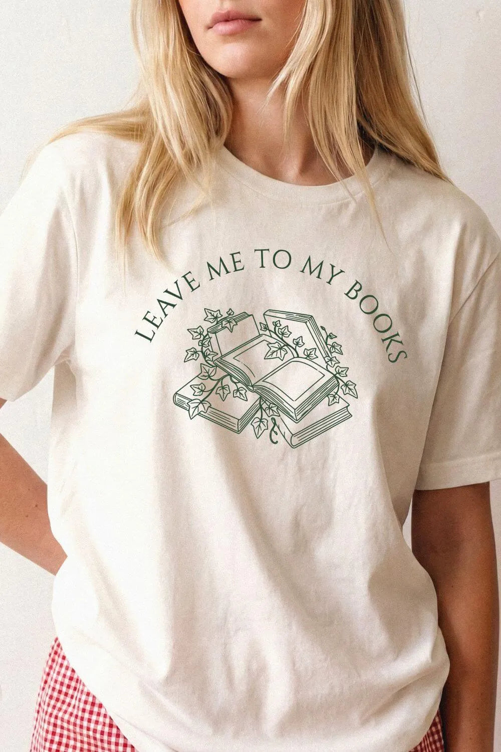 woman wearing a natural beige  bookish t-shirt with “Leave Me To My Books” text and vintage books illustration, styled as  introvert aesthetic outfit for cozy reading days