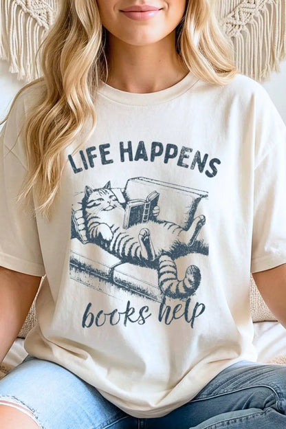 Model wearing funny bookish t-shirt with cat reading illustration and “Life Happens Books Help” text, styled as soft neutral outfit for relaxed reading days