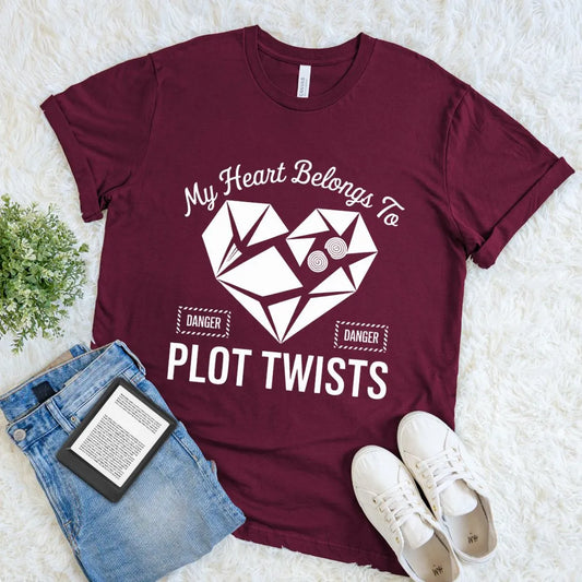 Flat lay of maroon red  reader tee featuring bold graphic heart and literary phrase "my heart belongs to plot twists"