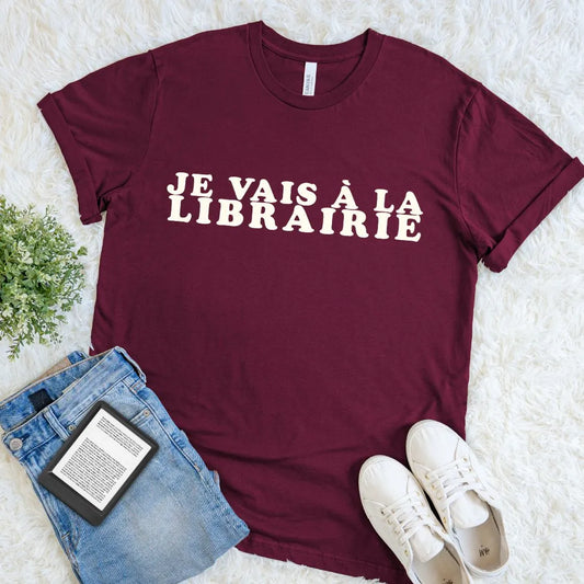 Maroon French reader shirt with oversized cream Je Vais à La Librairie typography, paired with cuffed jeans, sneakers, and a digital book