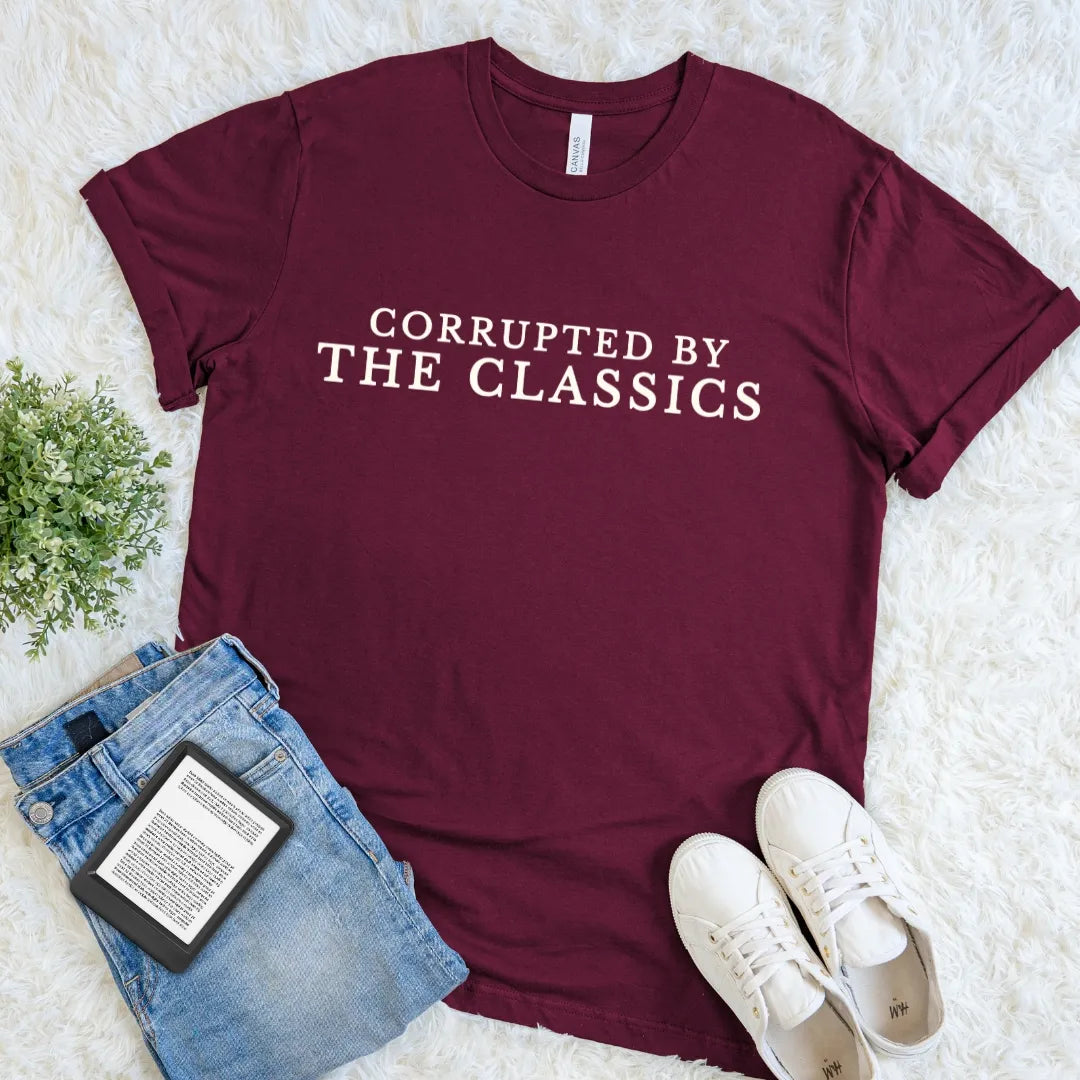 Maroon bookish T-shirt for classic literature readers with Corrupted by the Classics text  paired with jeans and sneakers on a light background.