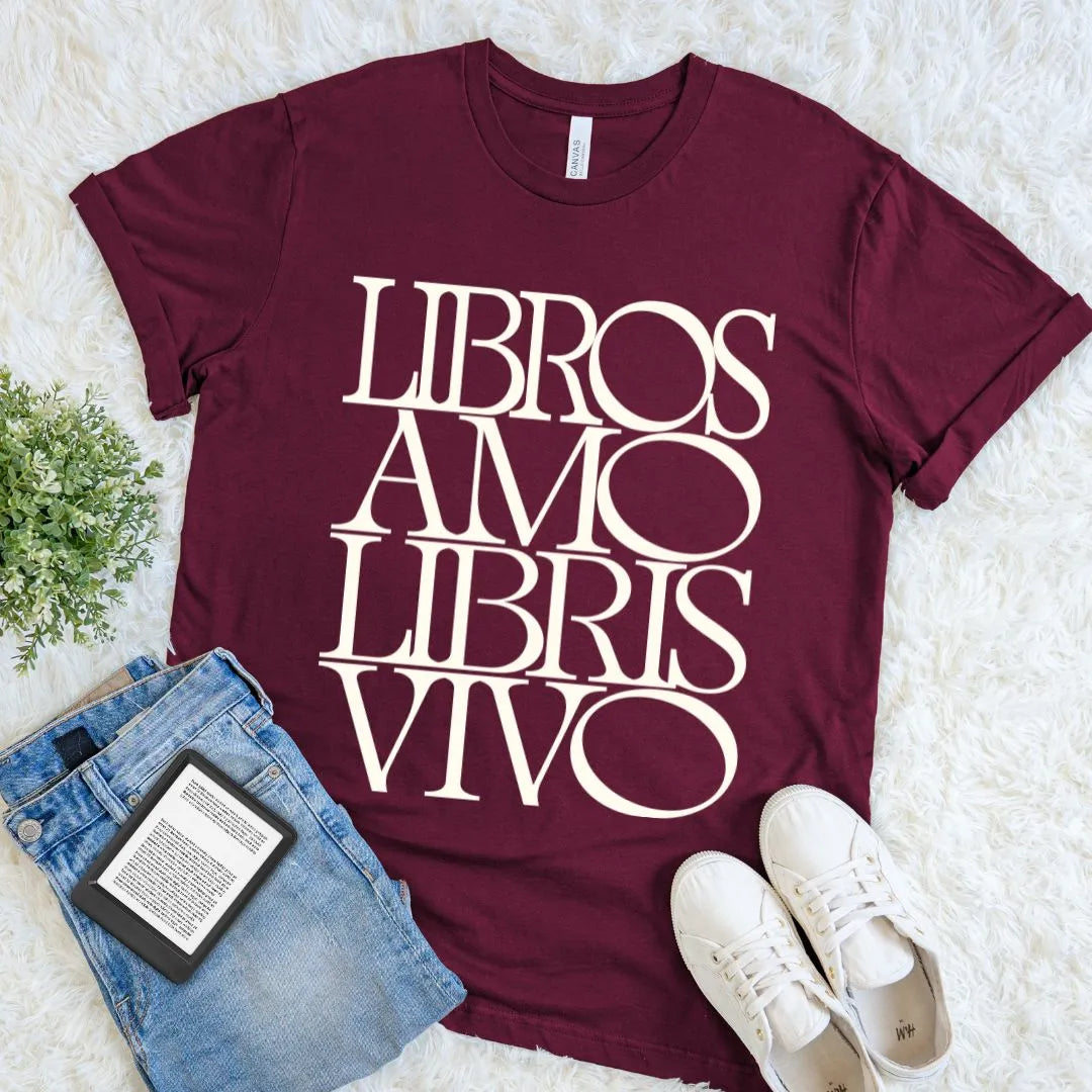 Maroon literary graphic tee with oversized cream Libros Amo Libris Vivo typography, arranged beside jeans, an e-reader, and sneakers