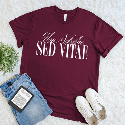 Soft cotton maroon red t-shirt with dark academia motto 'Non Scholae Sed Vitae', paired with jeans and sneakers on a light background for casual chic look